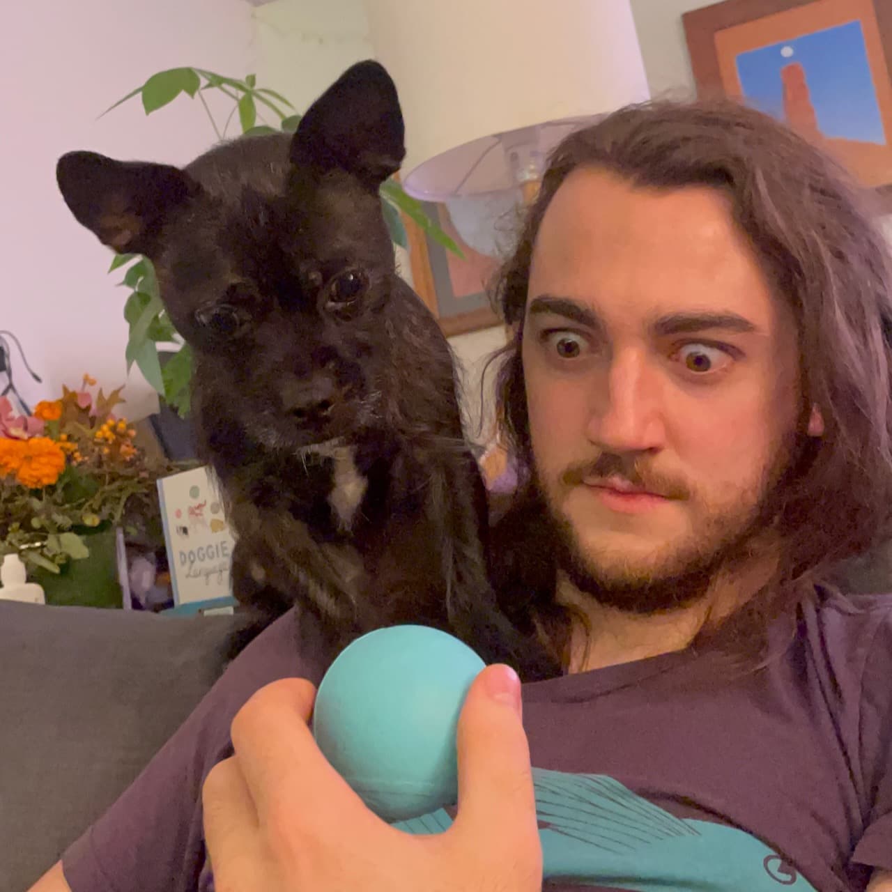 A photo of me staring at a ball with bulging eyes while my dog Orzo sits on my shoulder doing the same thing.