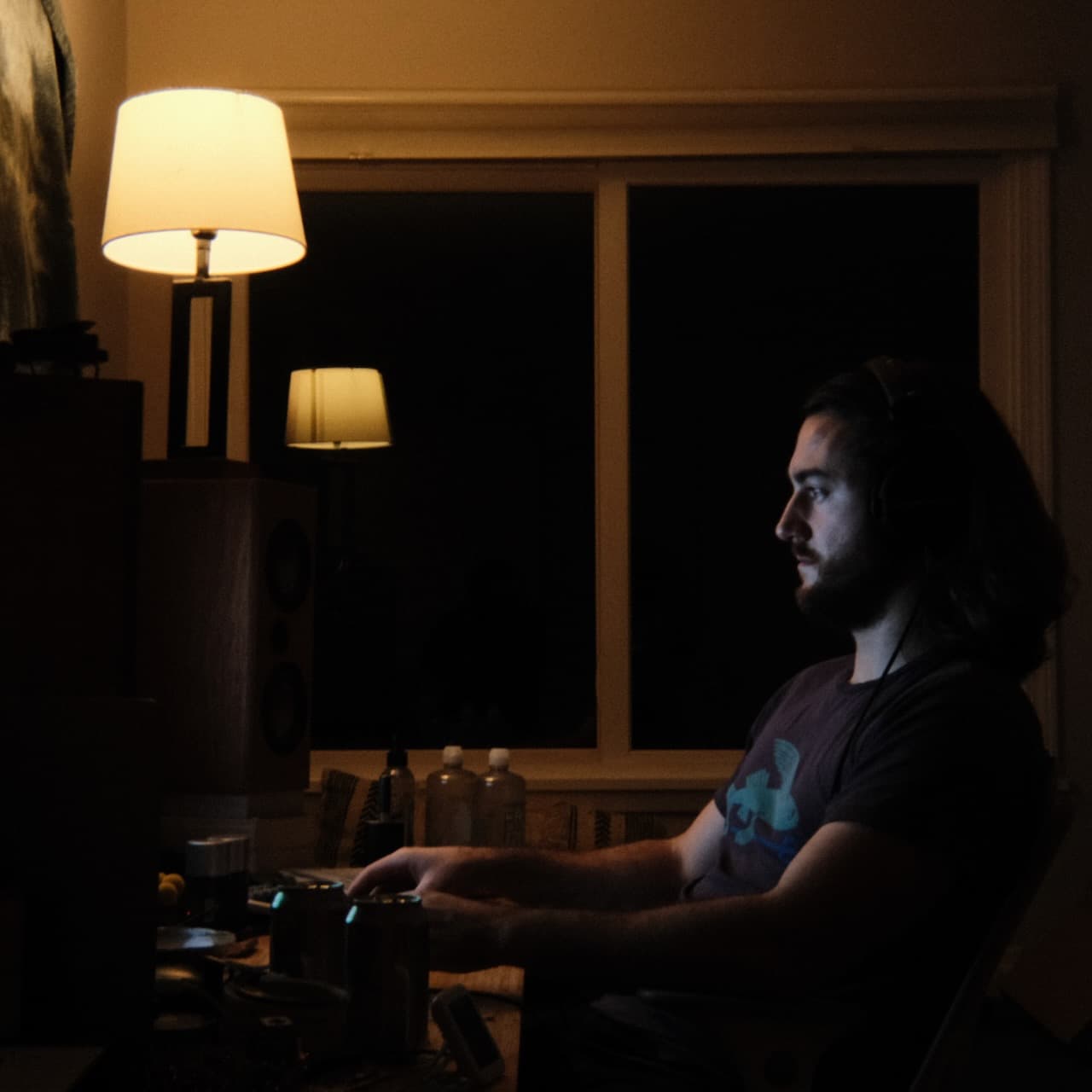 A photo of me sitting at a desk at night, lit by the backlight of a monitor hidden behind a set of speakers.